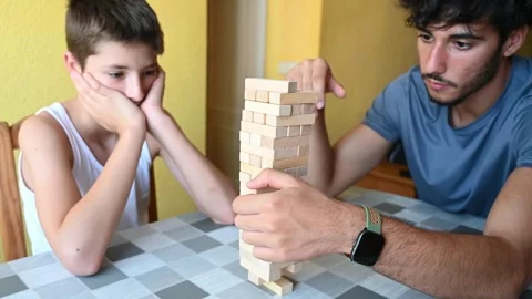 Brothers playing board game building a tower of wooden pieces, logic game Stock Footage 343218690