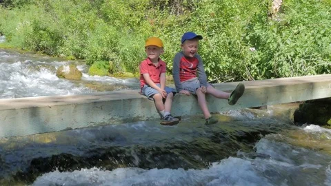 Brothers sitting on a bridge over a small mountain river. Stock Footage 77996039