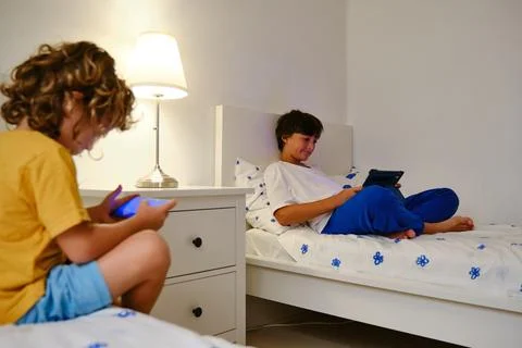 Brothers using gadgets in bedroom Stock Photos