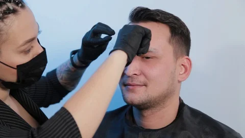 Browist makes eyebrow correction with a thread to a man in a beauty salon. Stock Footage 130082854