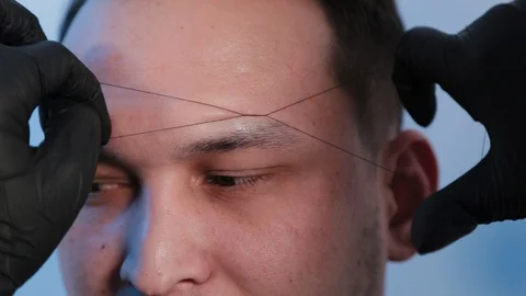 Browist makes eyebrow correction with a thread to a man in a beauty salon. Stock Footage 130082943
