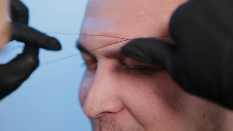 Browist makes eyebrow correction with a thread to a man in a beauty salon. Stock Footage 130083055