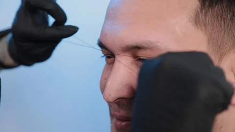 Browist makes eyebrow correction with a thread to a man in a beauty salon. Stock Footage 130083094