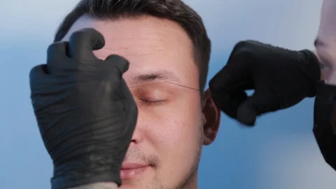 Browist makes eyebrow correction with a thread to a man in a beauty salon. Stock Footage 130083361