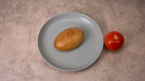 On a brown background, a red tomato and a bun move towards a plate. Stock Footage 309100666