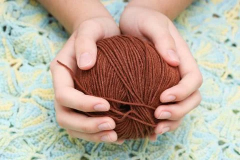 Brown ball of wool in hands on the background of a knitted tablecloth Stock Photos