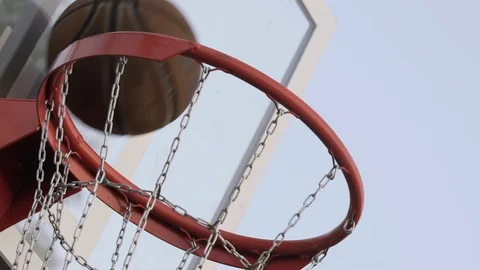 Brown basketball ball fall through basket with metal chain net on sunny summer Stock-Footage 129734798