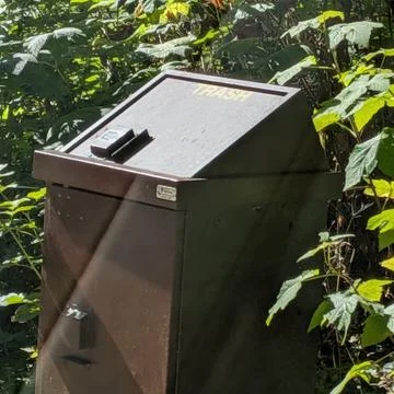 A brown bear-proof outdoor garbage can stands in a quiet forest park Stock Photos
