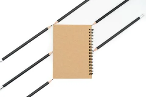 This brown book is placed between 6 black pencils and all on a white backgrou Stock Photos