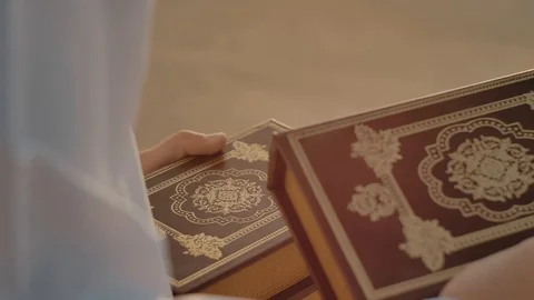 Brown books with a gold pattern in the hands of a Caucasian man in white clothes Stock Footage 105674828