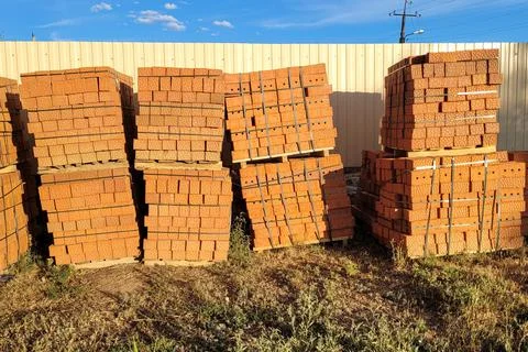 Brown bricks stacked on pallets along construction site fence Stockfoto's