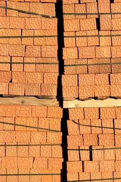 Brown bricks stacked on pallets along construction site fence Stockfoto's