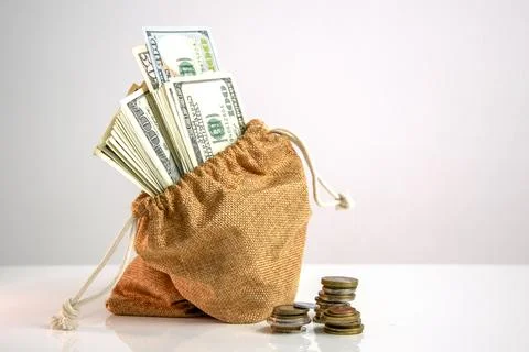 A brown burlap sack filled with stacks of US dollar bills sits on a white s.. Stock Photos
