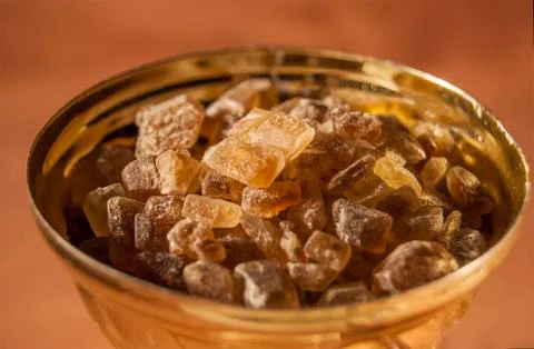 Brown cane sugar is lumpy inside the bowl of the golden cup. Stock Photos