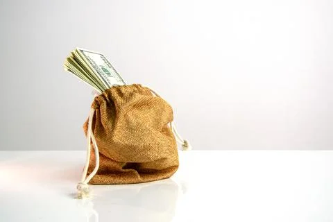 A brown canvas bag with a drawstring sits on a white surface. Several US do.. Stock Photos