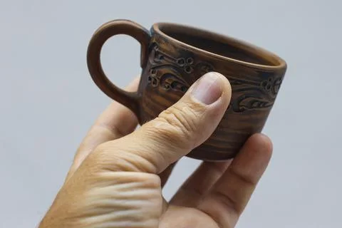Brown ceramic cup in hand on a light background. Stock Photos