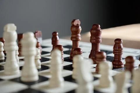 Brown chess pieces facing white pieces on chessboard Stock Photos