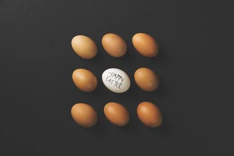 Brown chicken eggs flat lay on black background with one white Happy Easter.. Stock Photos