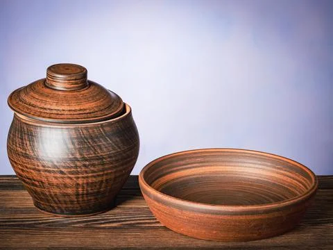 Brown clay pot with empty plate on wooden board Stock Photos