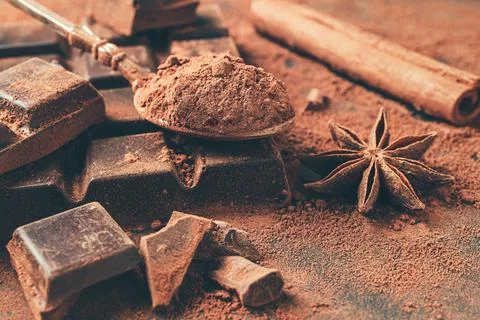 Brown cocoa powder in the spoon, chopped chocolate cubes, cinnamon stick Stock Photos