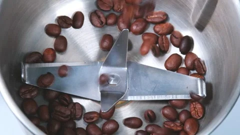 Brown coffee beans fall into metal shredder with sharp knives, silver-colored co Stock Footage 247176987