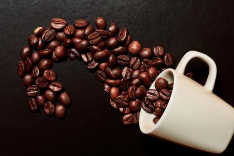 Brown coffee beans scattered on the table from the white espresso cup Stock Photos