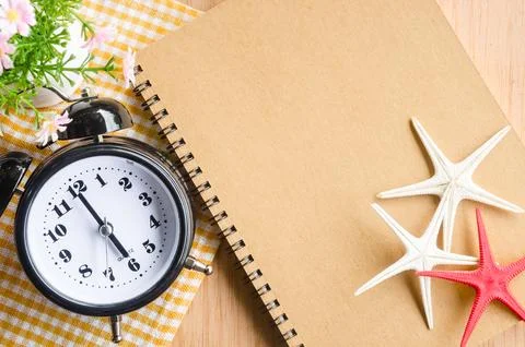 Brown diary and alarm clock with flower on wooden background. Stock Photos