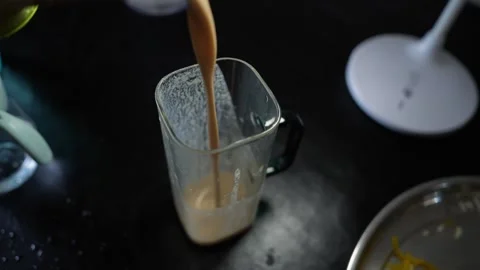 Brown drink being poured into a blender cup on a dark kitchen counter, with.. Видео 339022479