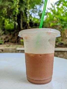 Brown drink in a plastic cup with a straw. on a white table Stock Photos