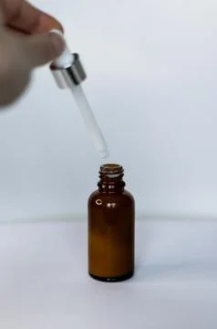 Brown dropper bottle without label, human hand holding pipette with white serum Foto stock