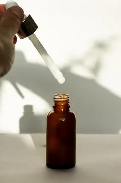 Brown dropper bottle without label, human hand holding pipette with white serum Stock Photos