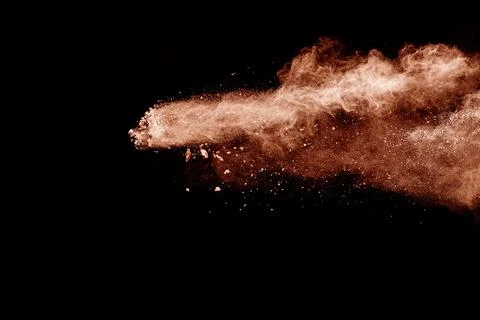 Brown dust explosion cloud.Brown particles splatter on black background. Stock Photos