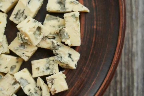 Brown earthenware plate on which close-up of blue dor blue cheese, cut into cube Stock Photos
