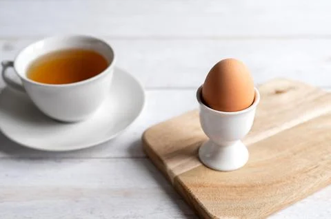 Brown egg in ceramic egg cup on wooden board with cup of tea. Healthy breakfast Stock Photos