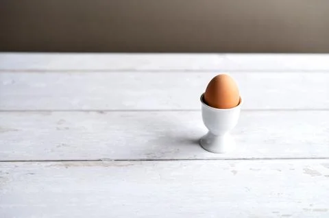 Brown egg in a ceramic egg cup placed on a white wooden table. Concept healthy Stock Photos