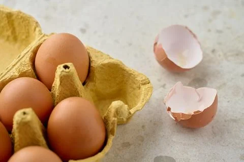 Brown eggs in carton with broken eggshells on kitchen table 스톡 사진