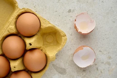 Brown eggs in carton with cracked empty shells on kitchen surface Stock Photos