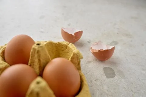 Brown eggs in carton with cracked empty shells on kitchen surface Stock Photos