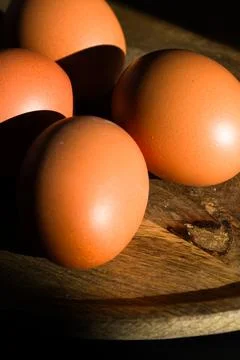 Brown Eggs on Wooden Surface in Dramatic Low-Key Lighting Stock Photos