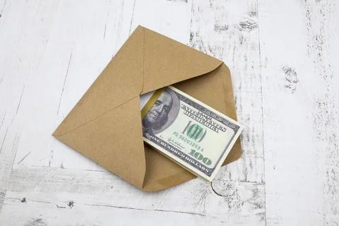 A brown envelope with a bundle of 100 dollars lies on a white wooden table 스톡 사진