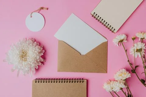 Brown envelope, tag, notebook with blank card and flower on pink background Stock Photos