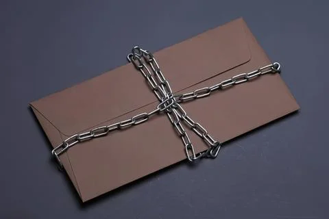 Brown envelope wrapped with metal chains on dark background Stock Photos