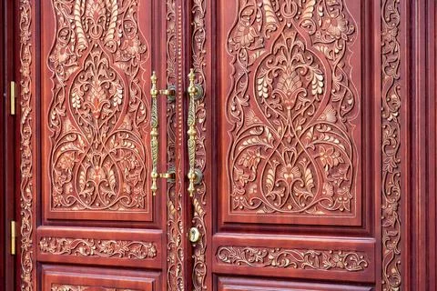 Brown front door with a pattern of wood carvings with iron handles. Stock Photos