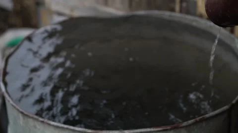 A brown gutter pipe empties rainwater into a brim-full metal barrel Stock Footage 344864239