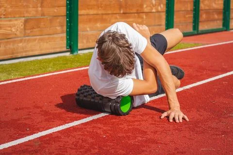 Brown-haired boy with an athletic physique on an athletic oval massages his m Stock Photos