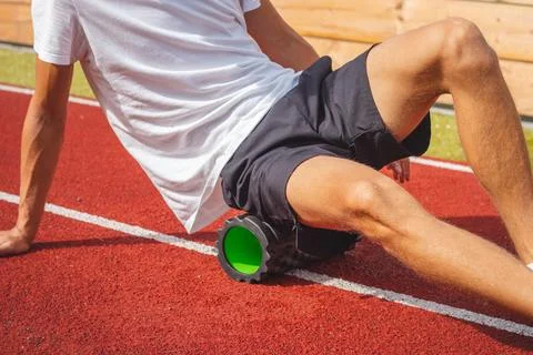 Brown-haired boy with an athletic physique on an athletic oval massages his m Stock Photos
