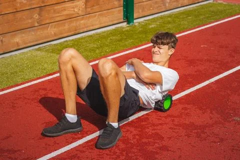 Brown-haired boy with an athletic physique on an athletic oval massages his m Stock Photos