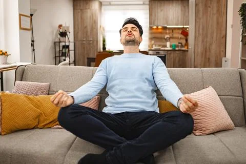 Brown-haired man sits on a couch and meditates Stock Photos