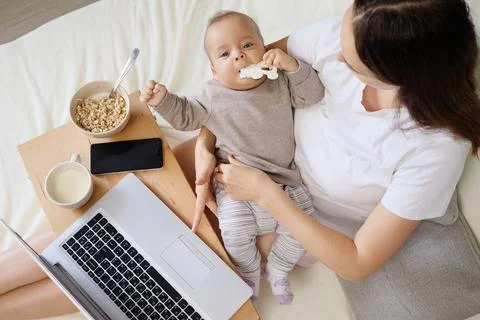 Brown-haired mother multitasking taking care of newborn and working on comp.. Stock Photos