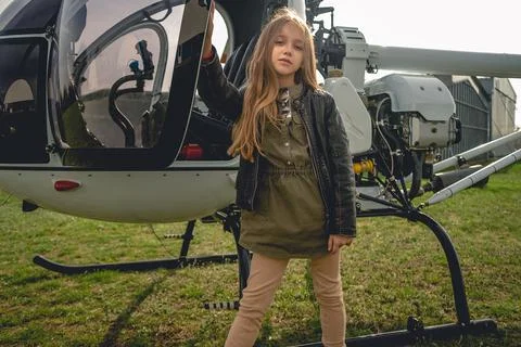 Brown-haired preteen girl standing near open helicopter Stock Photos